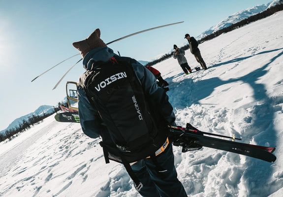 A skier walks towards a helicopter on the snow.