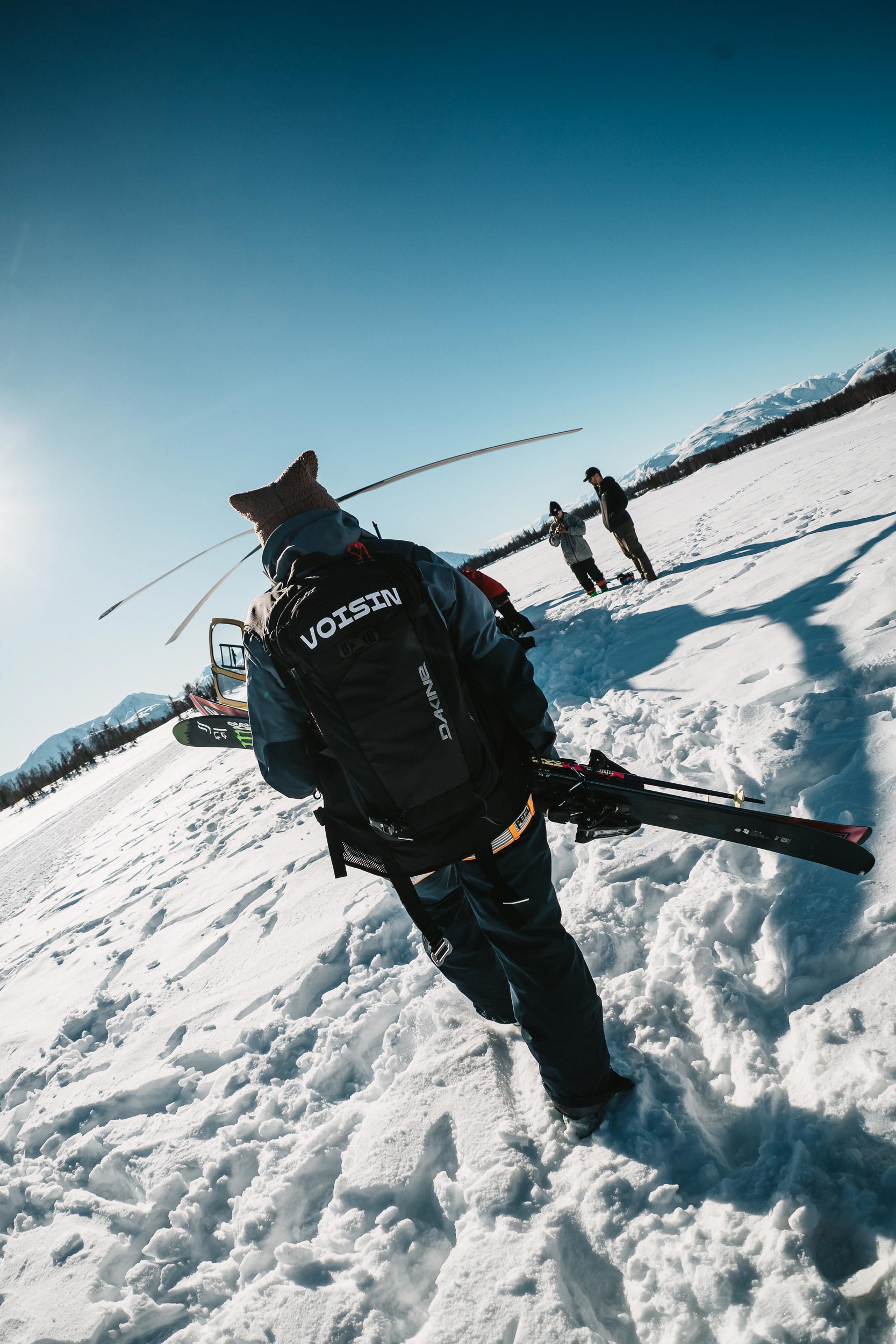 A skier walks towards a helicopter on the snow.