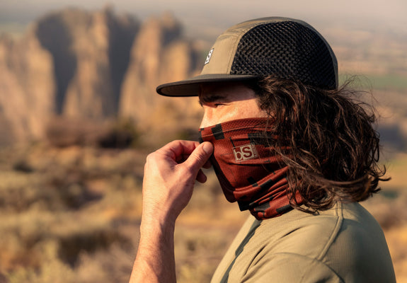 A man pulls up his neck gaiter up over his nose in the early morning light.
