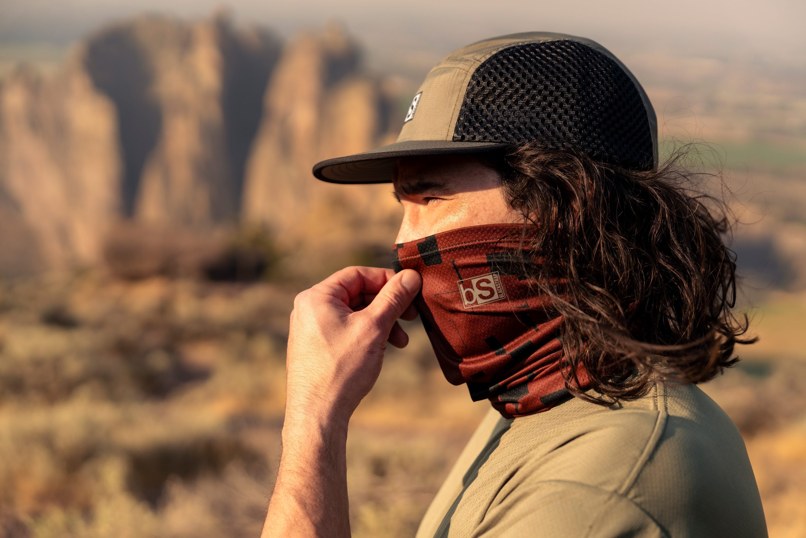 A man pulls up his neck gaiter up over his nose in the early morning light.
