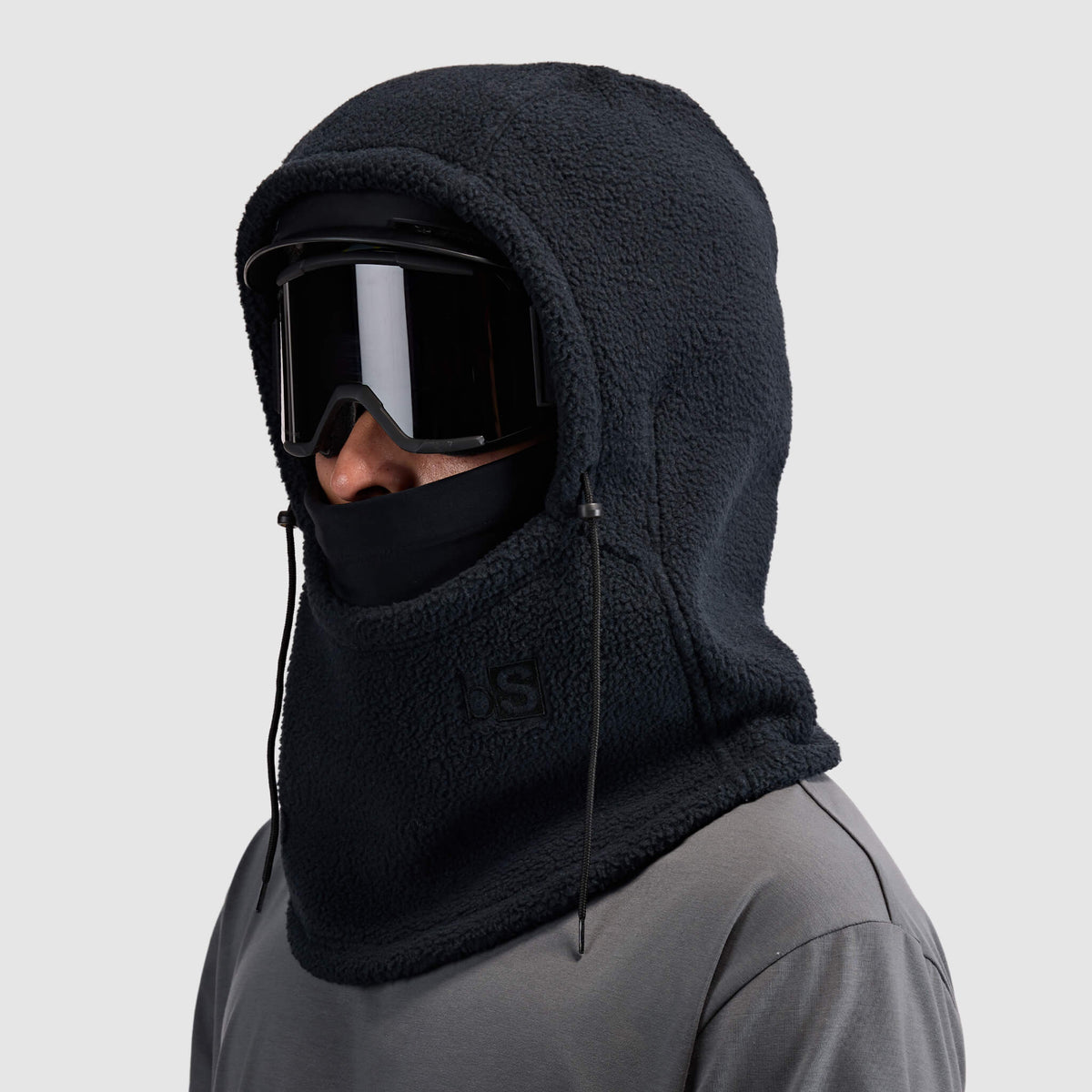 BlackStrap Caldera Hood Sherpa Fleece Overhood Black worn by a man wearing a helmet and ski goggles #color_black