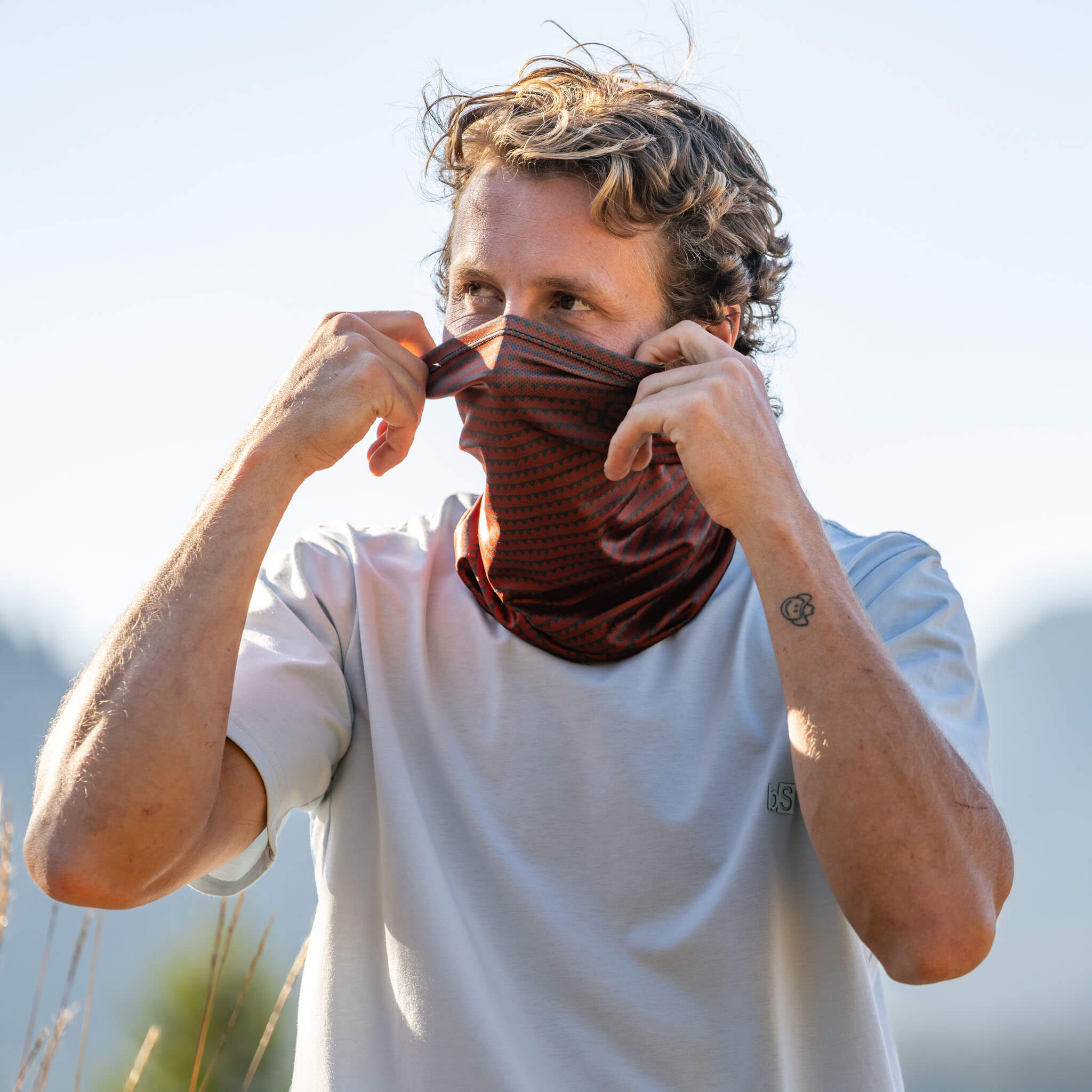 Man pulling a BlackStrap Daily Tube neck gaiter up over his face in an open meadow