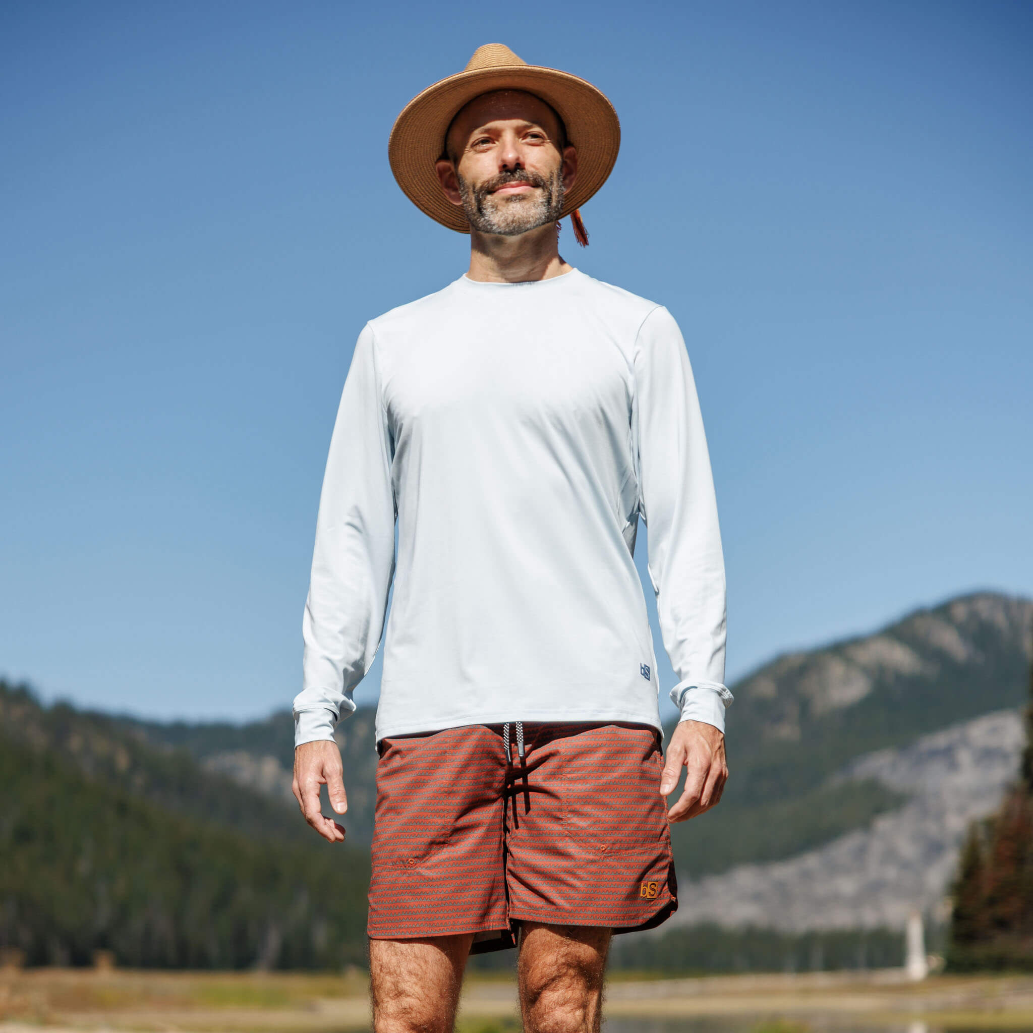 Man standing in an open mountain valley wearing the BlackStrap Men's Brackish Long Sleeve shirt #color_stratus