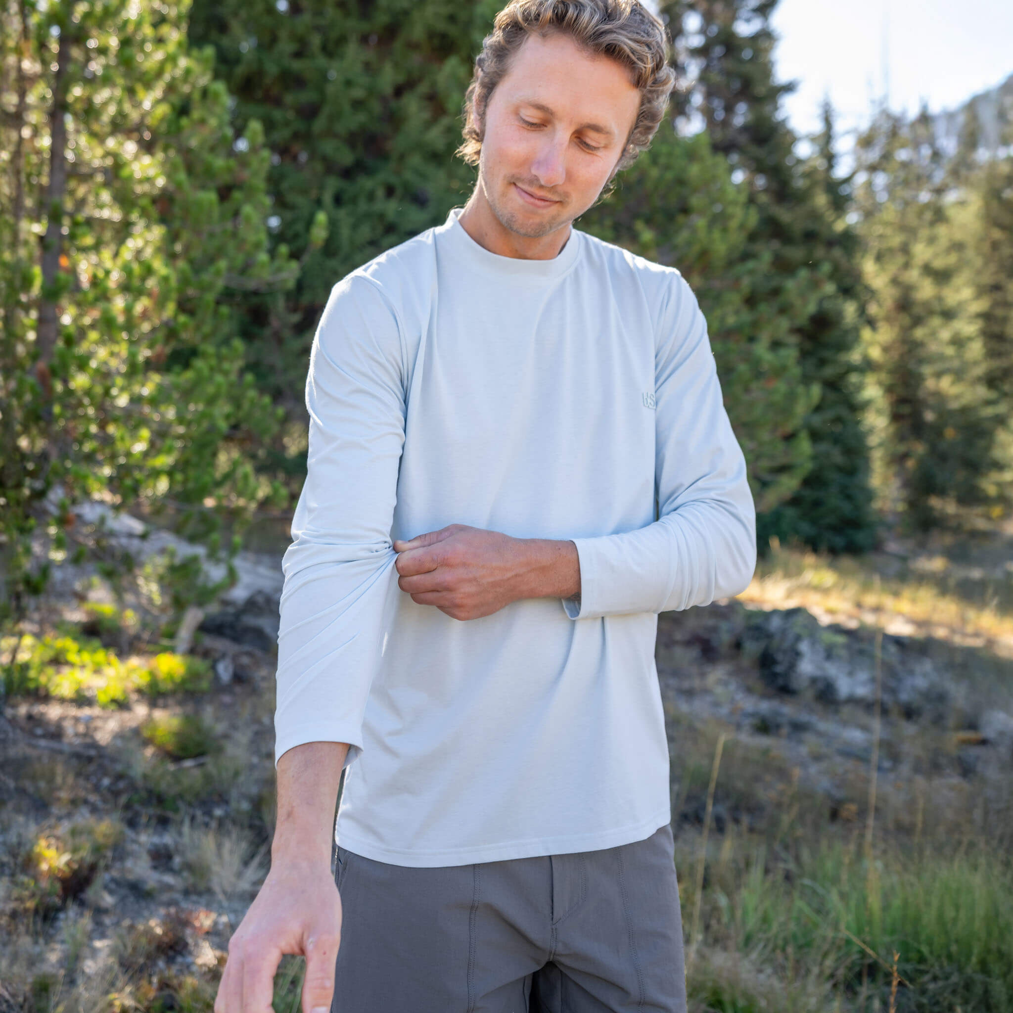Man adjusting his sleeve in an alpine pine forest wearing the BlackStrap Men's Voyage Crew Long Sleeve