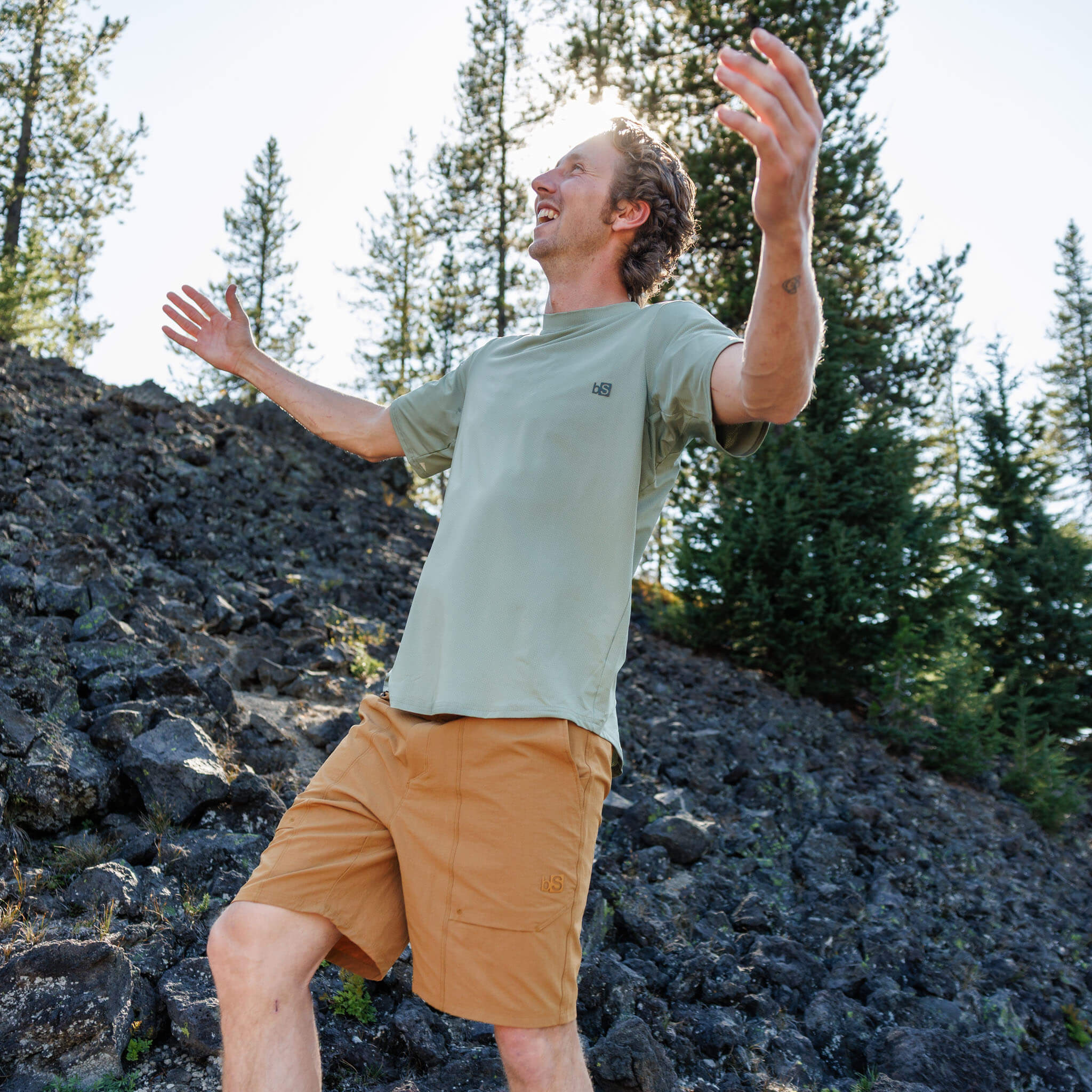 Man with arms raised on a volcanic rock hillside wearing the BlackStrap Men's Voyage Tee