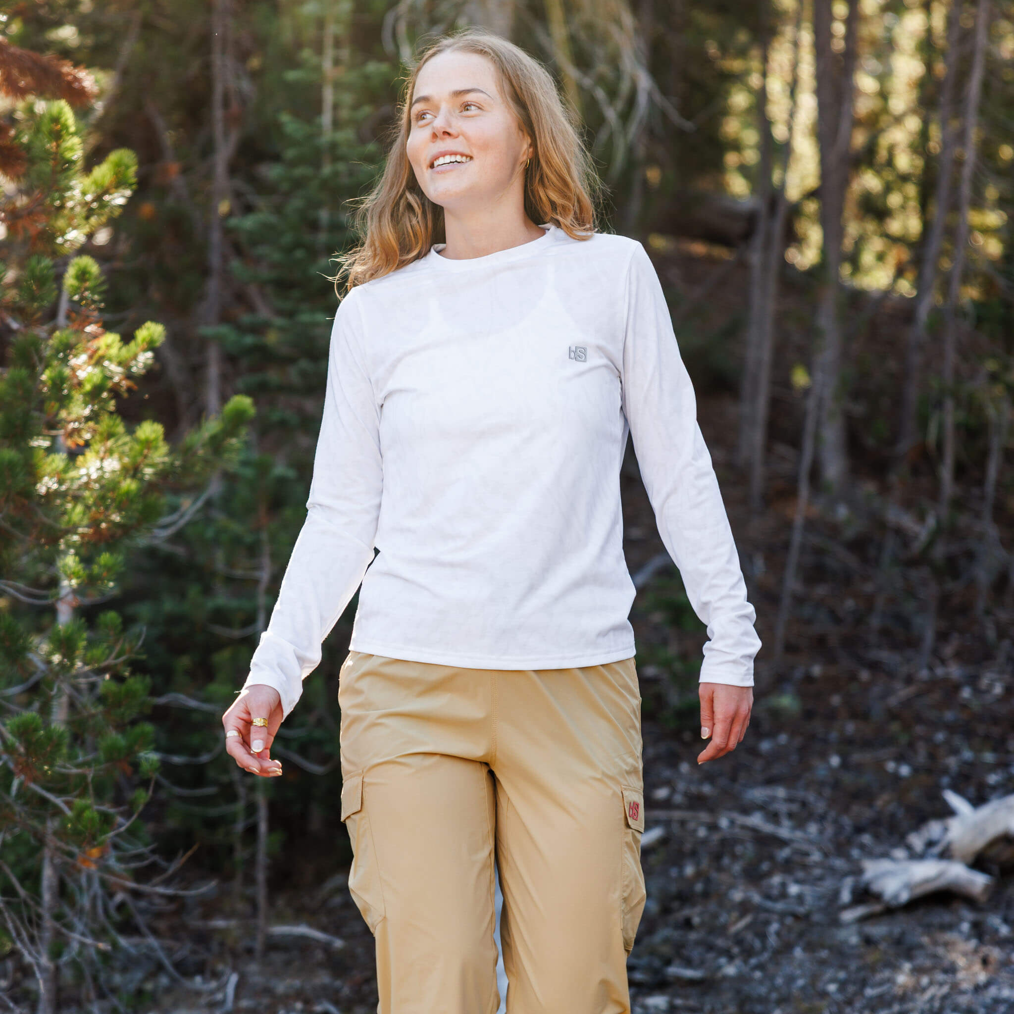 Woman walking through a pine forest wearing the BlackStrap Women's Aspect Long Sleeve #color_ripple ash