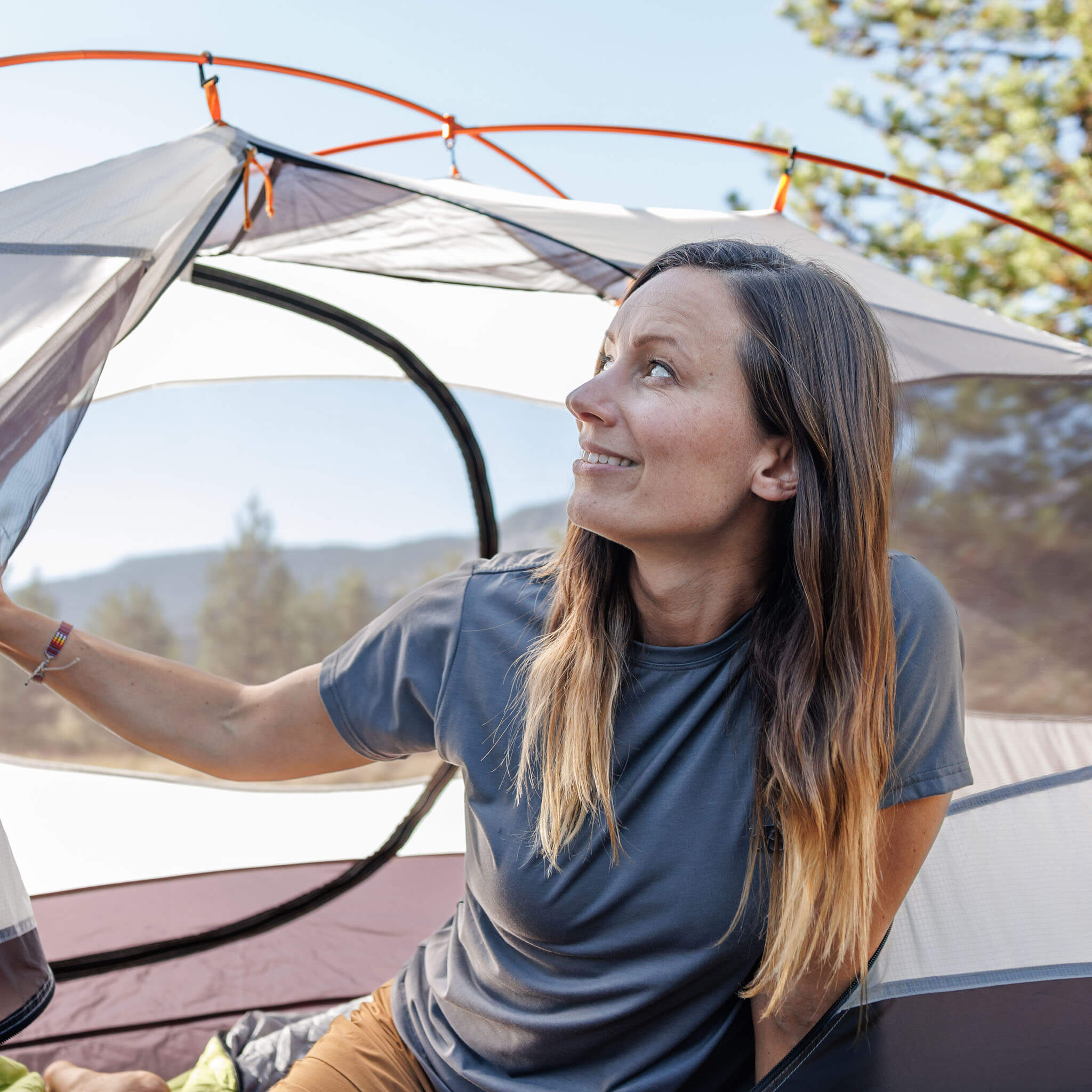 Woman setting up a tent at a mountain campsite wearing the BlackStrap Women's Aspect Tee #color_deschutes
