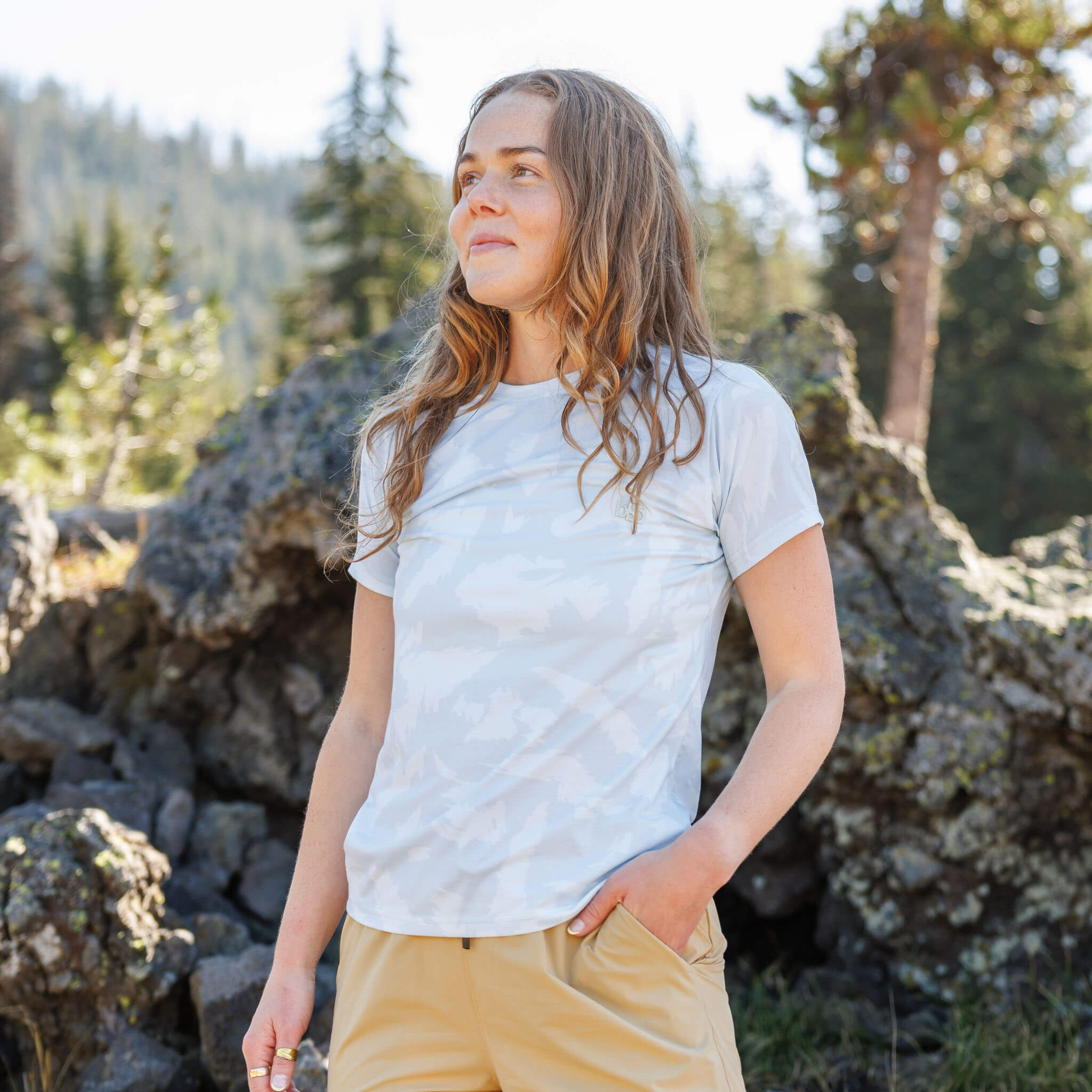 Woman standing among rocky alpine terrain wearing the BlackStrap Women's Aspect Tee #color_slash stratus