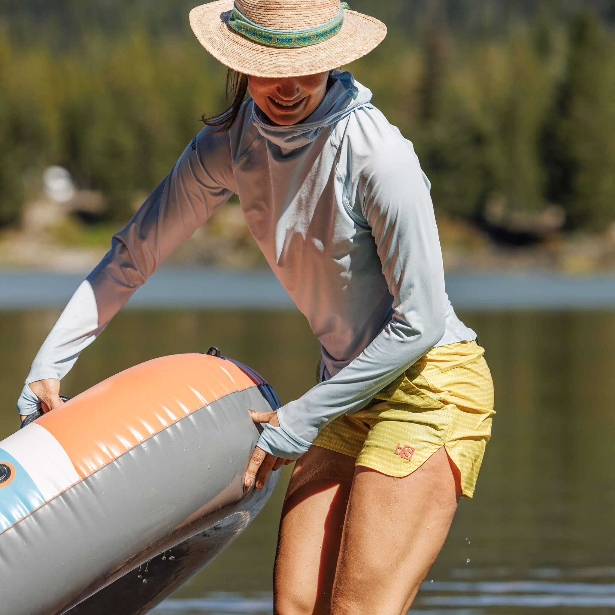 Woman pulling an inflatable tube out of a mountain lake wearing the BlackStrap Women's Brackish Long Sleeve Hoodie