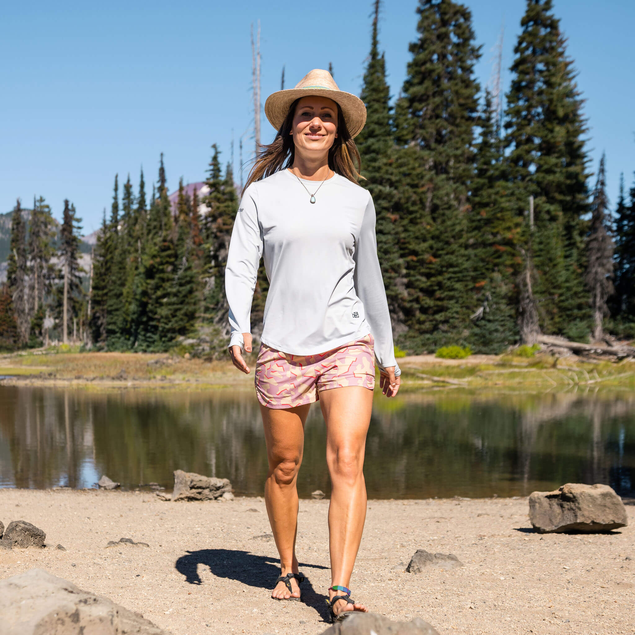 Woman walking along a sandy alpine lakeshore wearing the BlackStrap Women's Brackish Long Sleeve shirt #color_stratus
