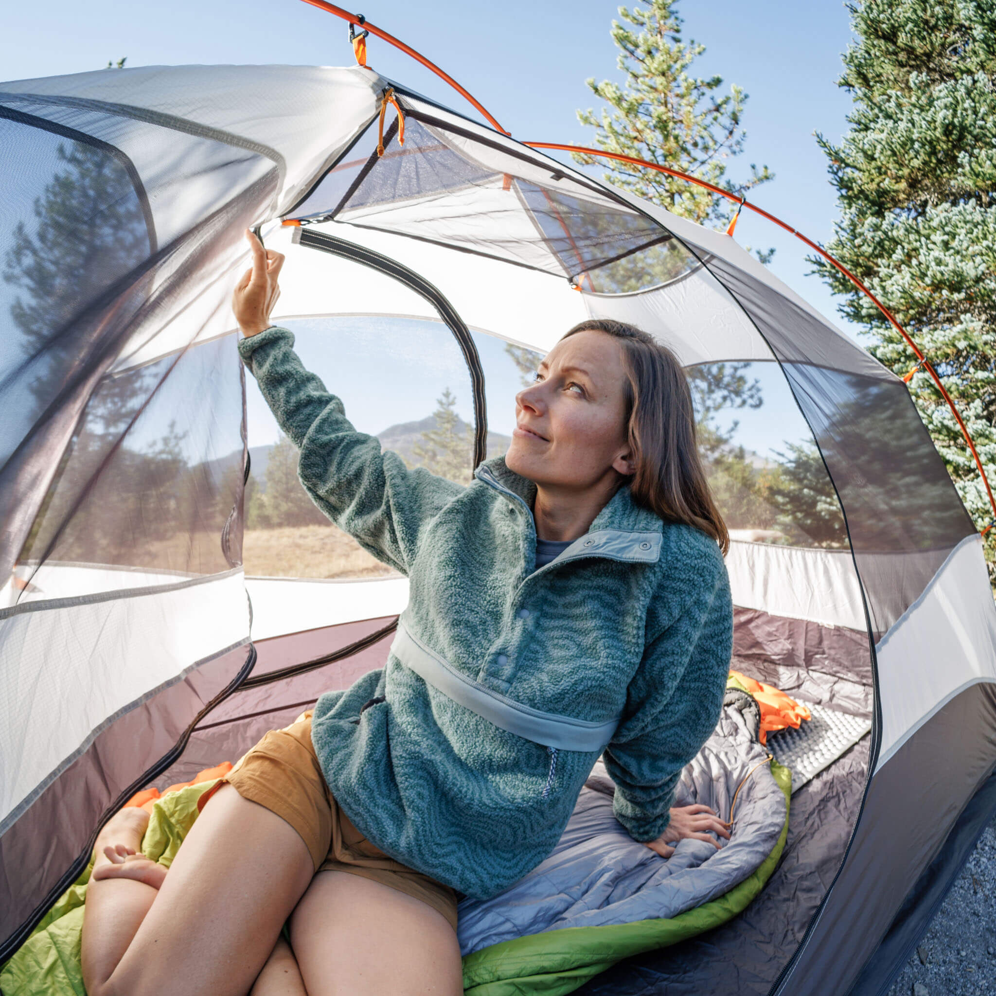 Woman sitting in a tent opening the rain fly wearing the BlackStrap Women's Caldera Sherpa Fleece Pullover #color_inprint-obsidian
