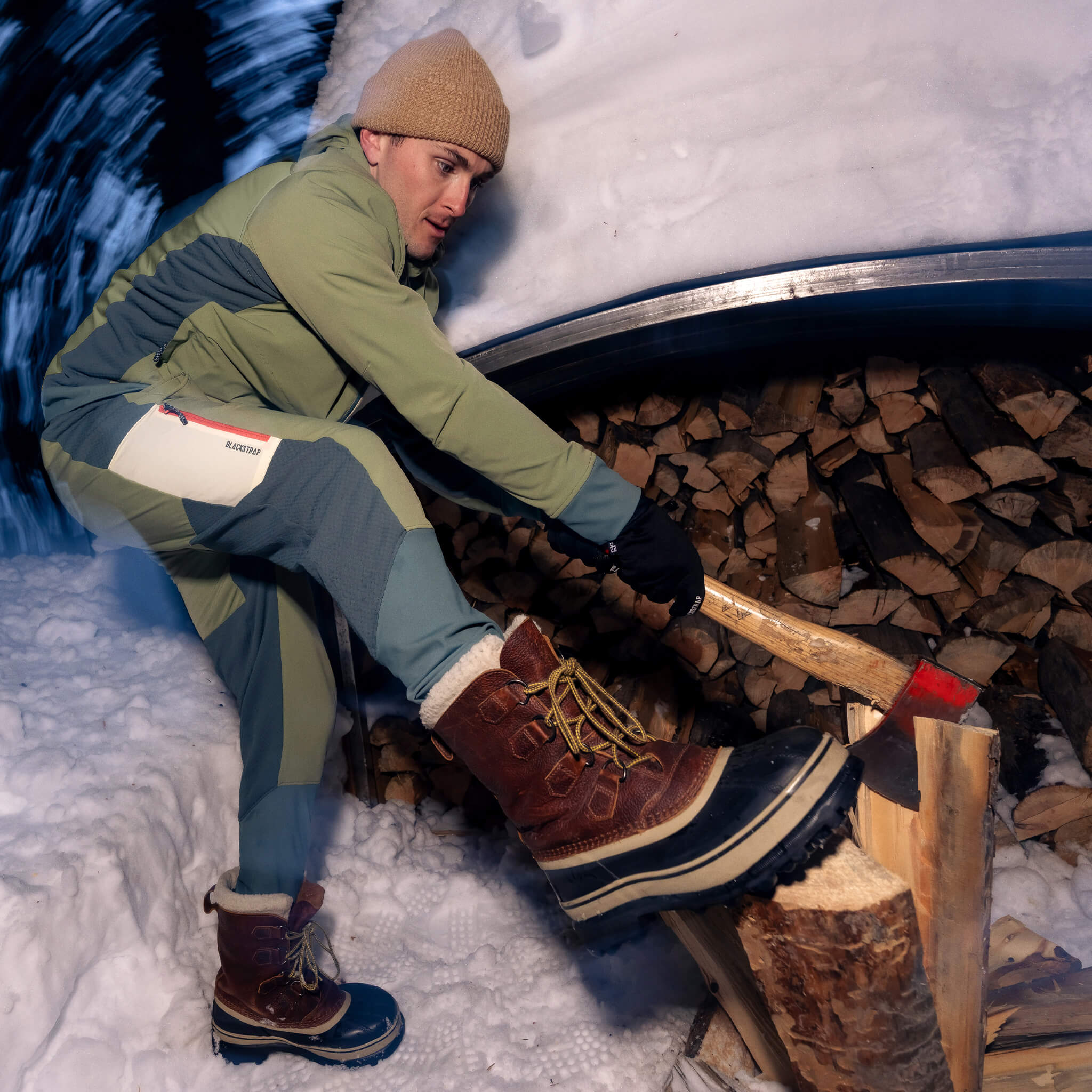 Male wearing the Tribrid hooded jacket and pants chopping firewood