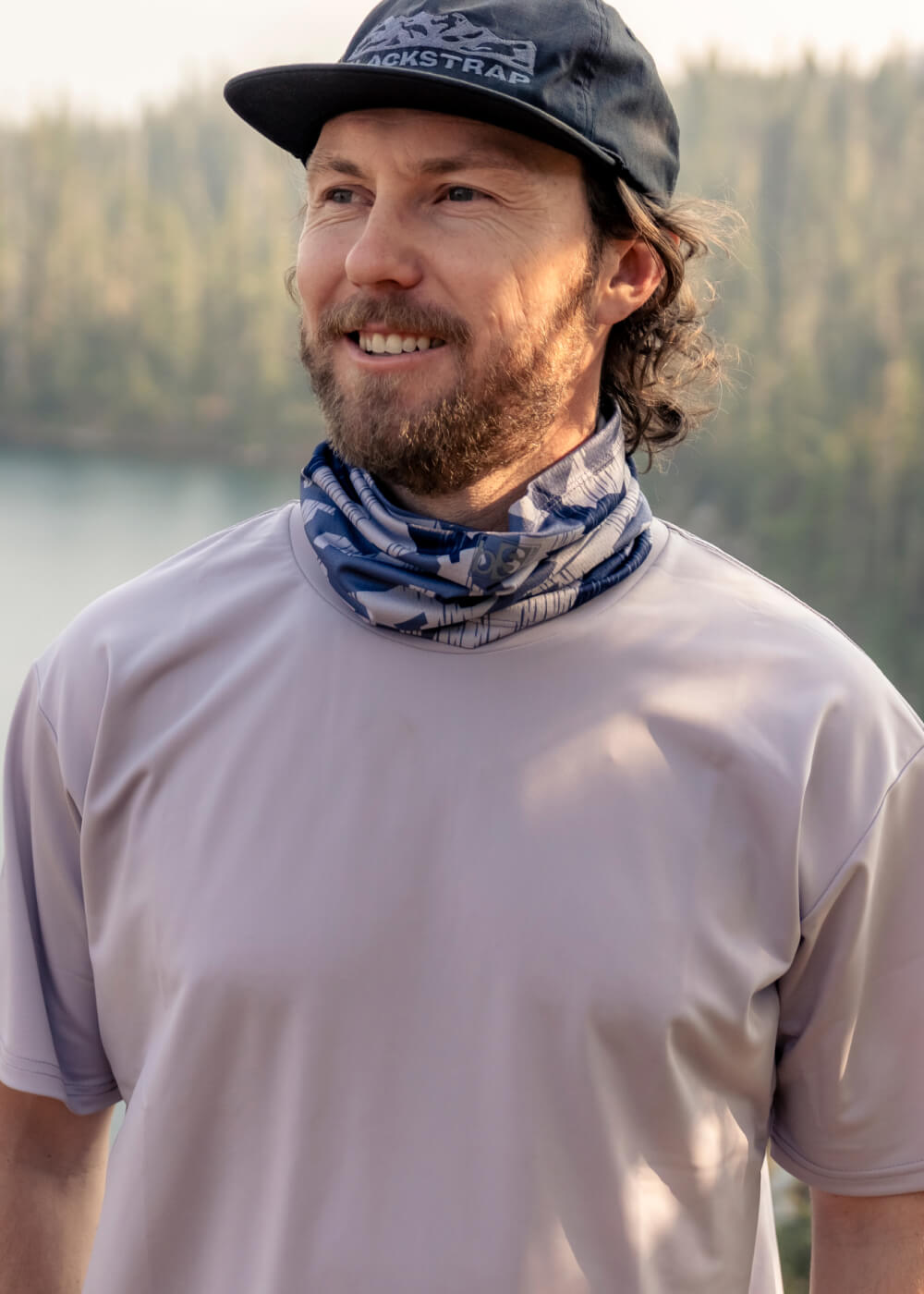 A hiker enjoying the view with a glassy lake behind him while wearing the BlackStrap Daily Tube