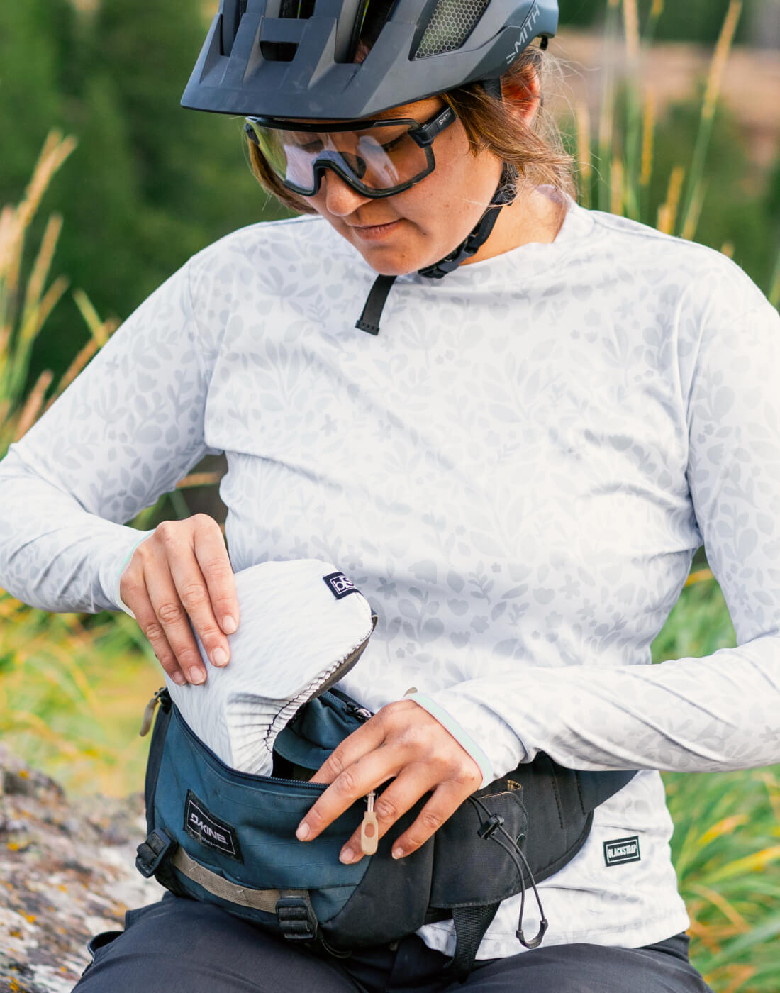 A biker throwing her BlackStrap goggle covers into a bag before enjoying the trail ahead.