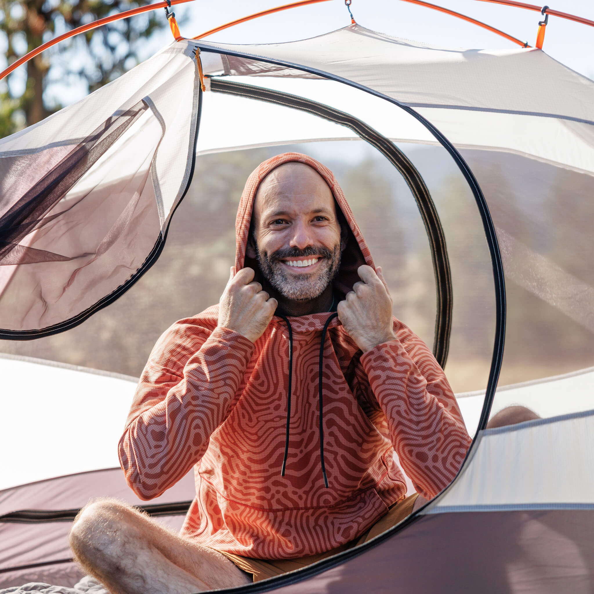 Man sitting inside a tent with a BlackStrap Baseleisure Hoodie on, smiling outdoors.  #color_inprint jory