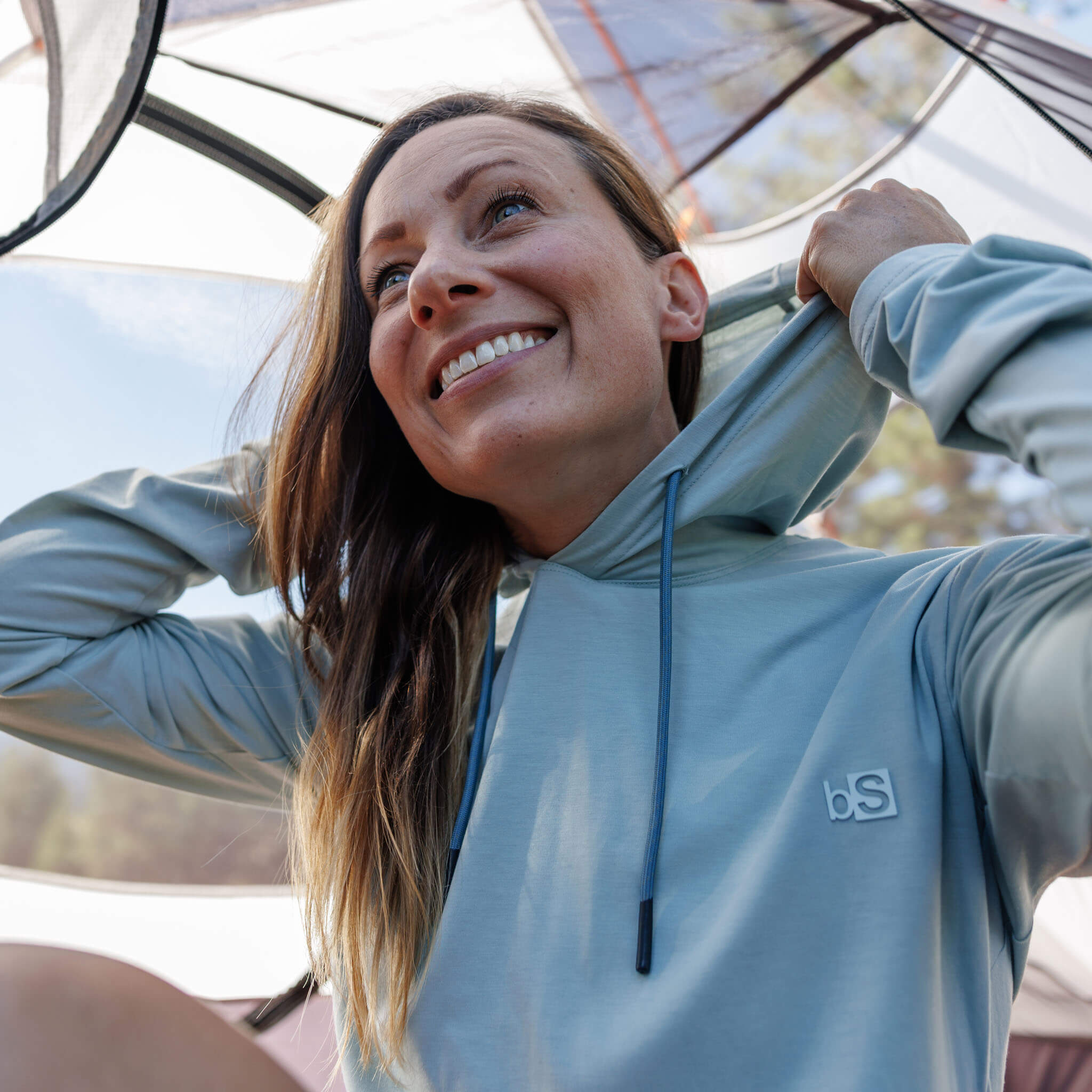 Woman setting up a tent wearing the BlackStrap Women's Aspect Hoodie Long Sleeve #color_spruce