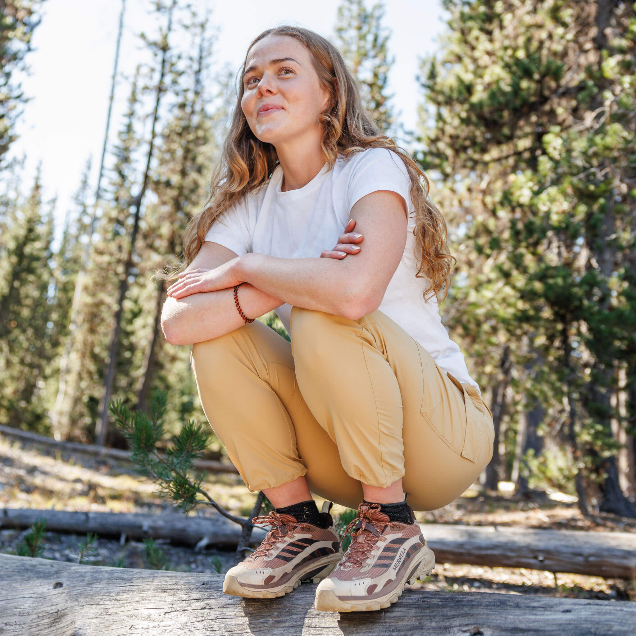 Woman crouching on a log in a pine forest wearing the BlackStrap Women's Aspect Tee