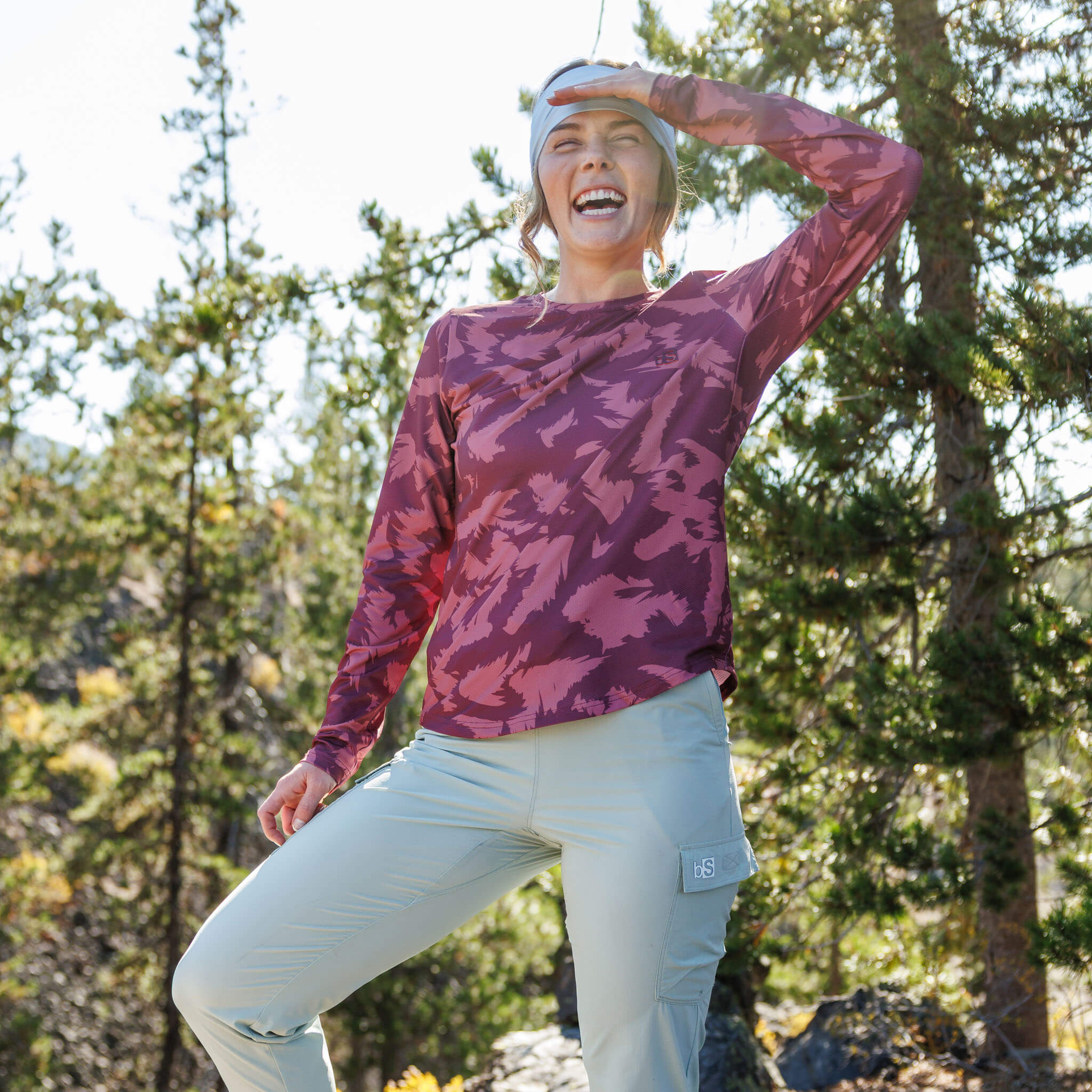 Woman balancing on one foot on a rocky mountain overlook wearing the BlackStrap Women's Voyage Crew Long Sleeve #color_slash cherry