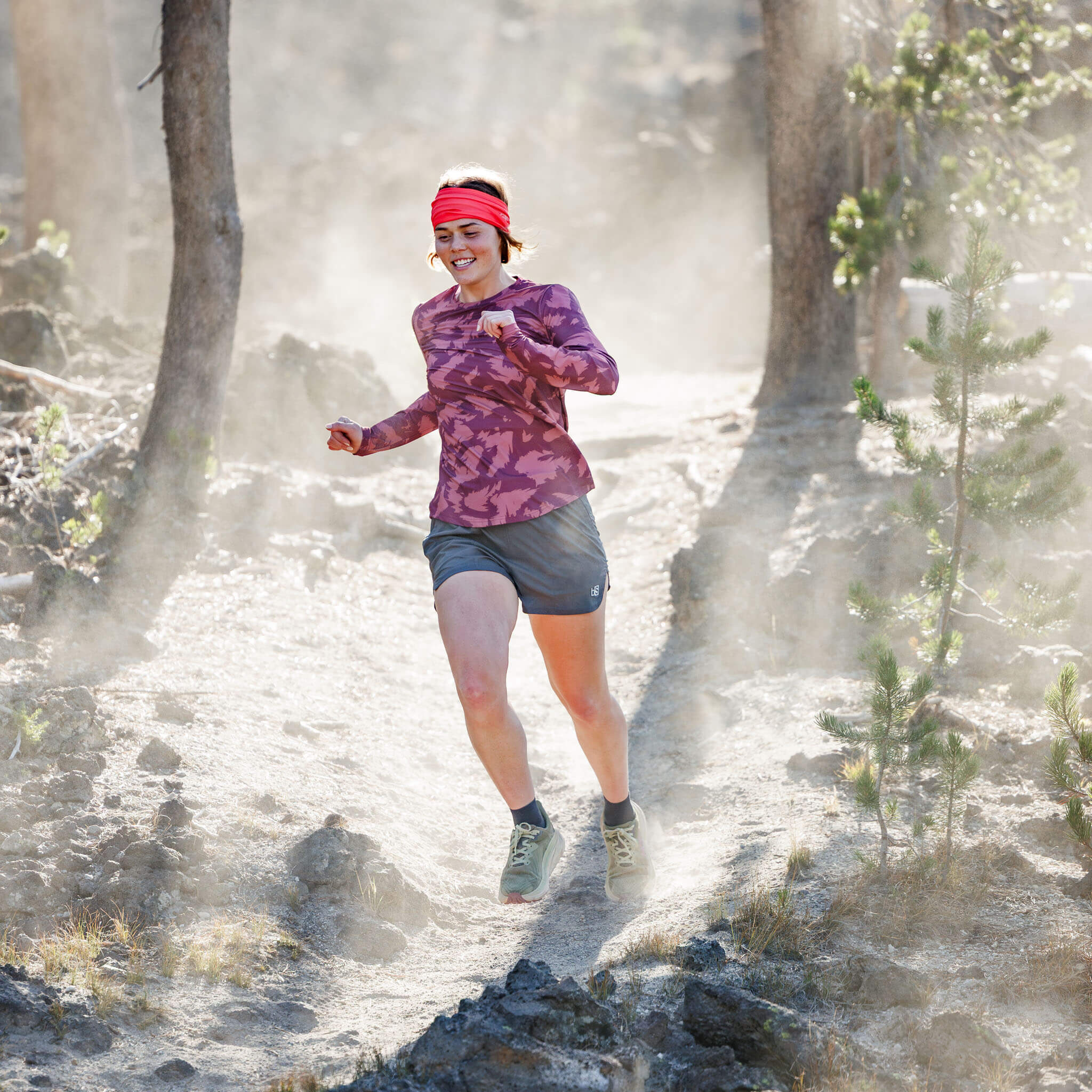 Woman trail running through a dusty pine forest wearing the BlackStrap Women's Voyage Crew Long Sleeve